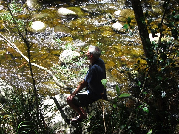 Man sitting beside flowing creek
